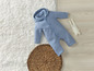 Ein blauer Baby-Overall mit Kapuze auf einem weißen Teppich.