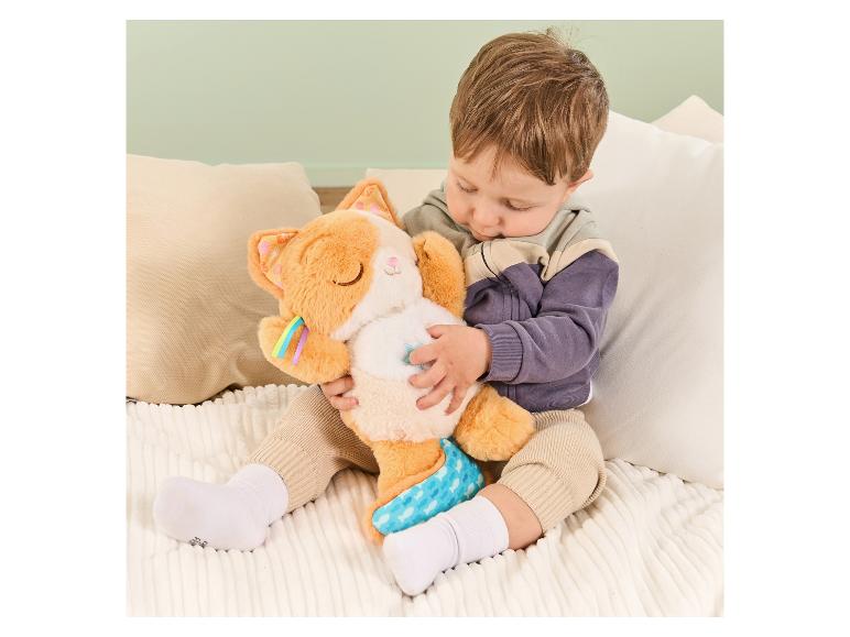 Baby spielt mit weichem orangefarbenen Katzenkuscheltier mit blauem Schwanz und Regenbogenstreifen.