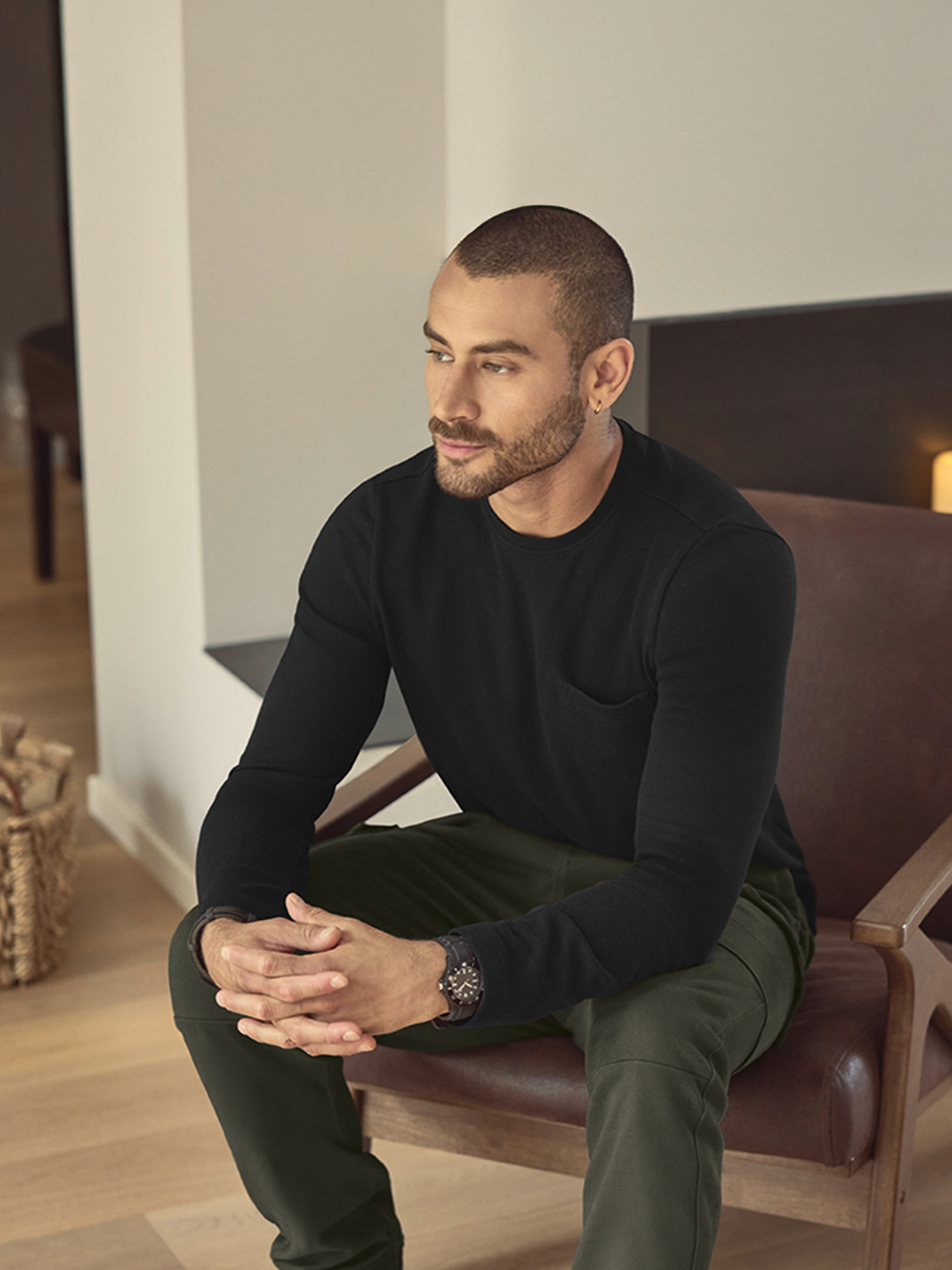 Mann in schwarzem Langarmshirt und grüner Hose, sitzt auf einem Ledersessel