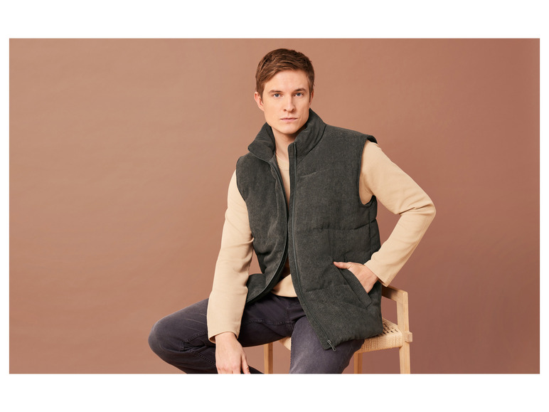 Ein Mann sitzt auf einem Holzstuhl und trägt eine dunkelgrüne Cordjacke.