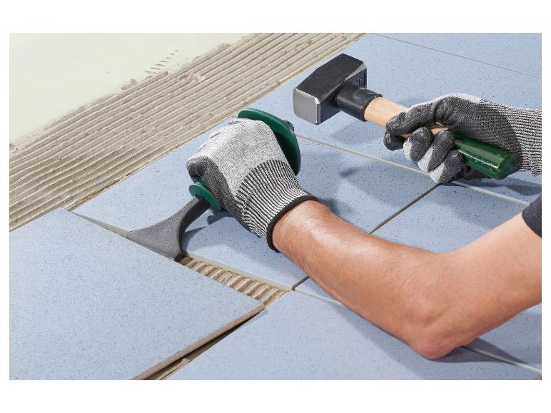 Mann verlegt Bodenfliesen mit Hammer und Verlegewerkzeug.