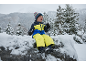 Kind in gelb-blauem Skianzug, Mütze und Handschuhen, sitzt auf einem verschneiten Felsen.