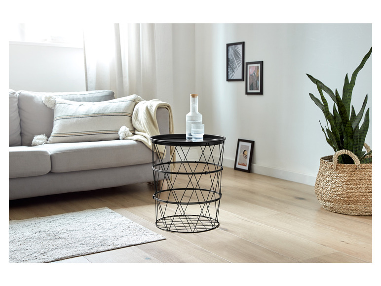 Ein schwarzer Metall-Beistelltisch mit einer Glasvase und einer Pflanze in einem Weidenkorb.
