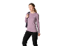Frau in lila Langarmshirt und schwarzer Hose, mit Rucksack auf der Schulter.