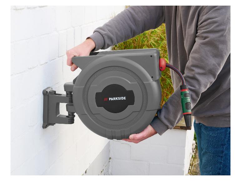 Mann montiert grauen Gartenschlauchaufroller an einer weißen Wand.