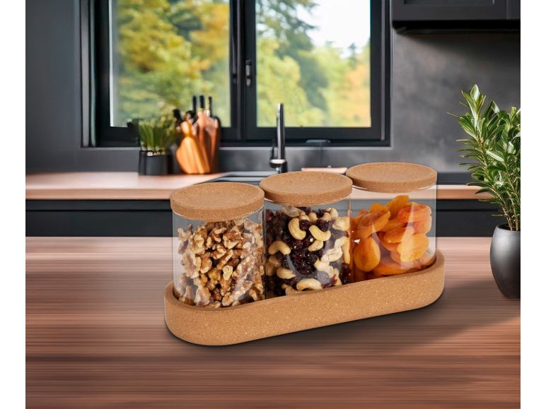 Korktablett mit Glasgefäßen, gefüllt mit Nüssen und Trockenfrüchten in einer Küche.