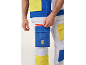Detail eines Mannes in weißer Weste und Hose mit blauen und gelben Taschen, der eine Tasche mit rotem Reißverschluss öffnet.