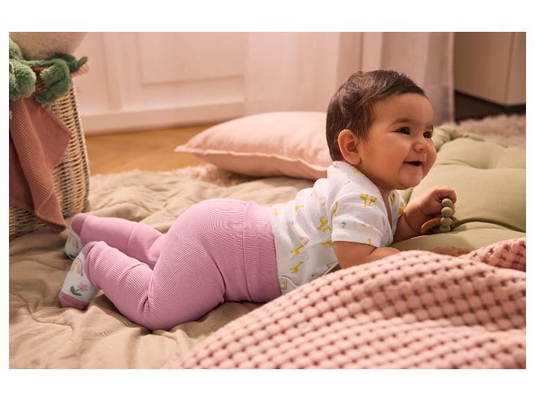 Lächelndes Baby in rosa Leggings und Giraffen-Body, auf dem Bauch liegend.