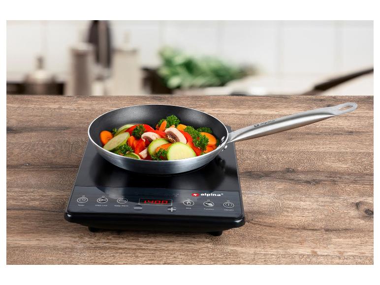 Induktionskochfeld mit Pfanne voller gehacktem Gemüse auf einem Holztisch.