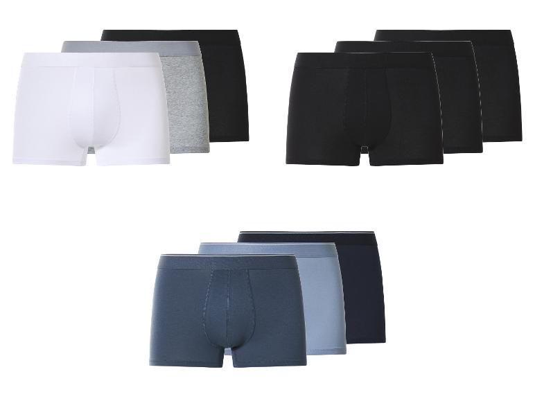 Drei Packungen Herren-Boxershorts in Weiß, Grau, Schwarz und Blautönen.