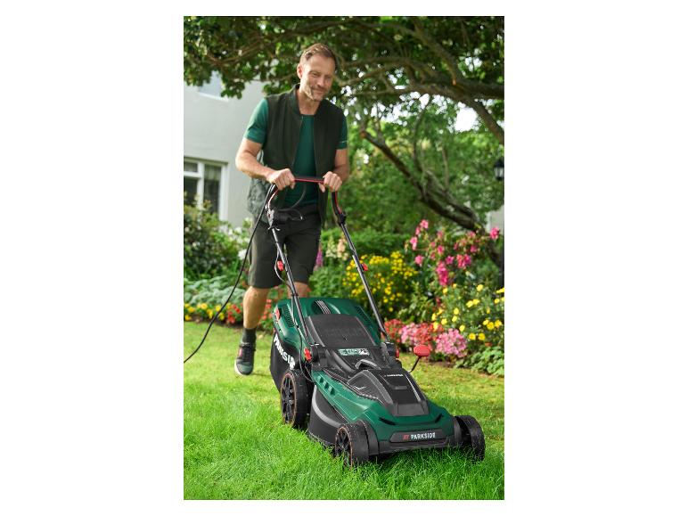 Mann mäht Rasen mit einem Parkside Elektro-Rasenmäher in einem blühenden Garten.