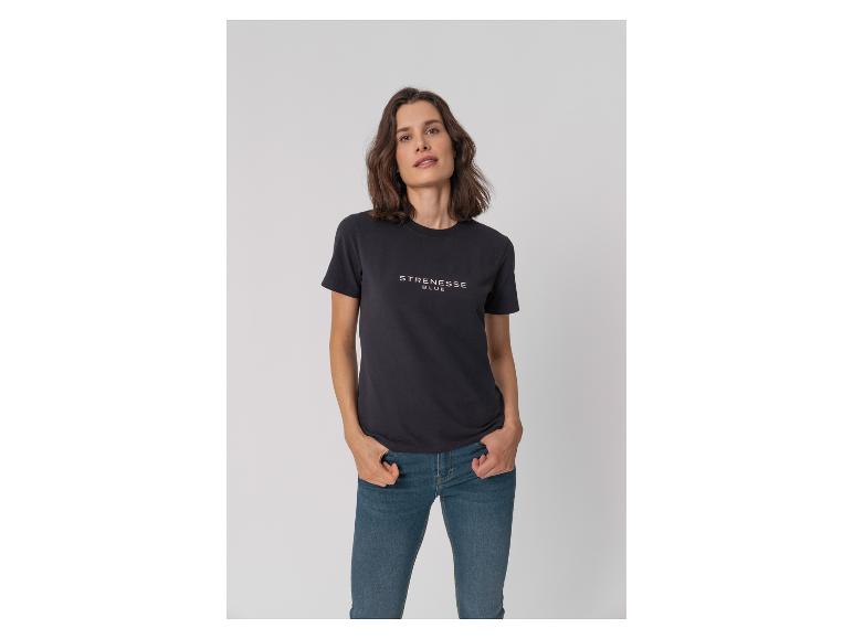 Frau in schwarzem T-Shirt mit Schriftzug und Jeans, Hände in den Taschen.