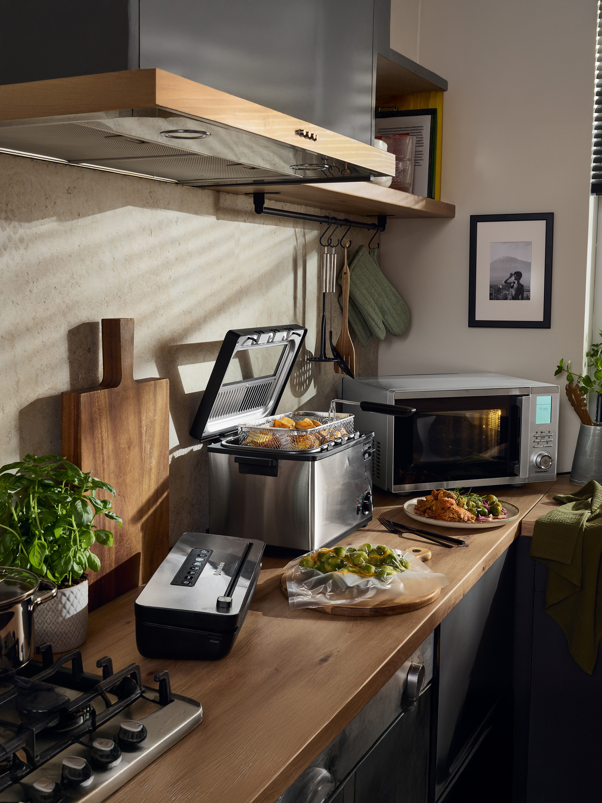 Küche mit Fritteuse, SilverCrest Mikrowelle, Vakuumiergerät und zubereitetem Essen.