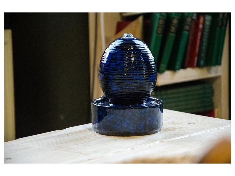 Blauer Keramik-Zimmerbrunnen auf einem Holztisch, mit Büchern im Hintergrund.