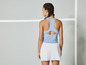 Eine Frau trägt ein hellblaues Tanktop und einen weißen Tennisskirt.