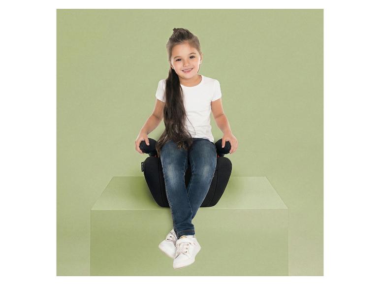 Lächelndes Mädchen sitzt auf einem schwarzen Autositz auf einem grünen Podest.