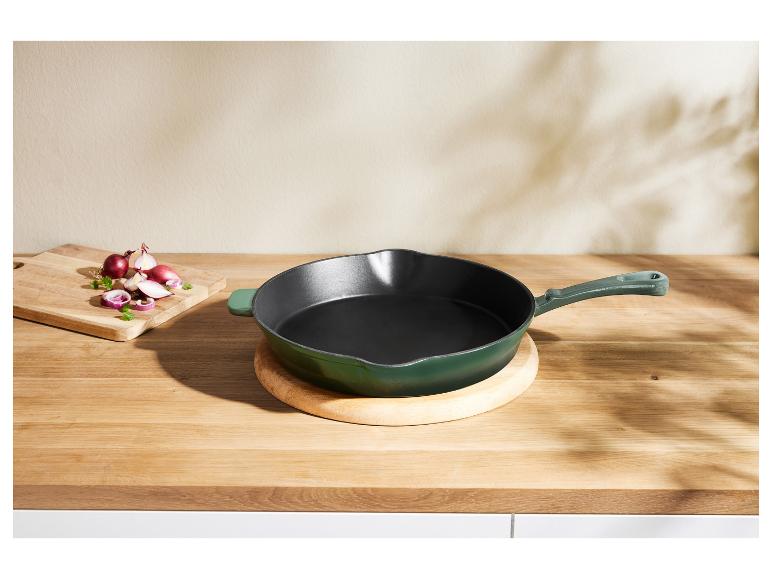 Grüne gusseiserne Staub-Pfanne auf einer Holztheke.