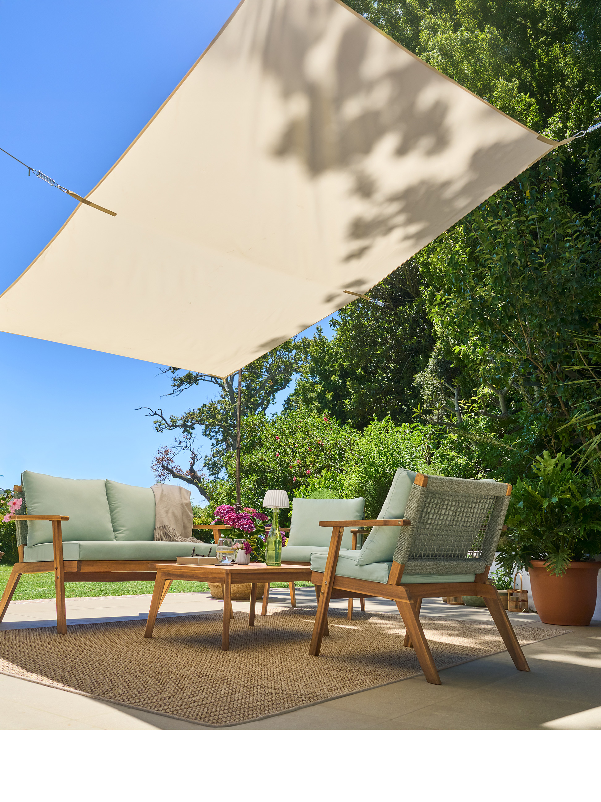 Holzsofa- und Sessel-Set mit grünen Kissen, Couchtisch und Sonnensegel auf einer Terrasse.