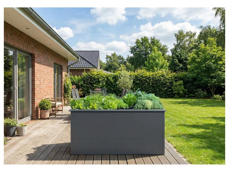 Graues Hochbeet mit frischem Gemüse auf einer Holzterrasse mit Garten.