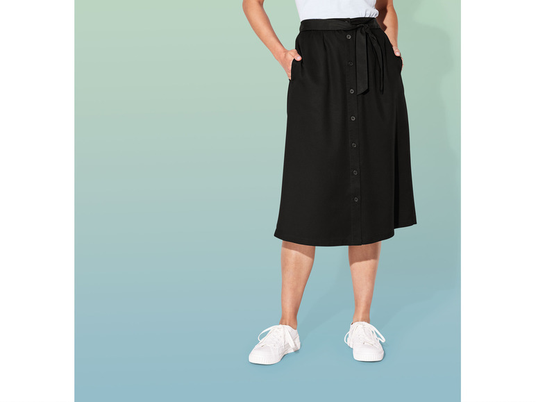 Eine Frau trägt einen schwarzen Rock mit Knöpfen und weiße Turnschuhe.