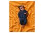 Baby in einem dunkelblauen Strickanzug, liegend auf einer orangefarbenen Decke.
