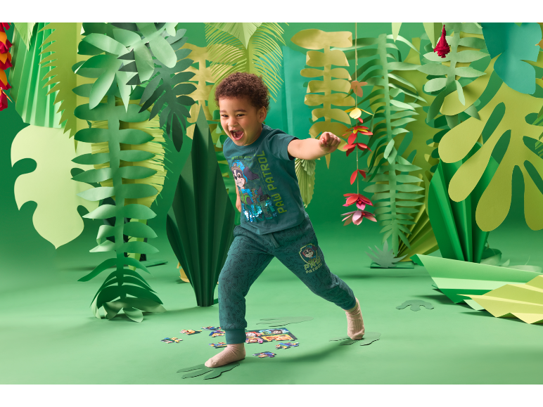 Kind spielt in einer grünen Dschungelumgebung, gekleidet in ein Paw Patrol Outfit.