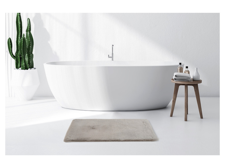 Eine freistehende Badewanne mit einem Badeteppich in einem modernen Badezimmer.