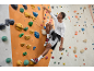Mann klettert an einer Kletterwand in einem Langarmshirt und sportlichen Shorts.