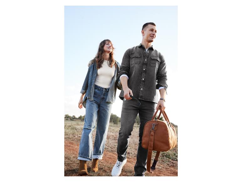 Ein Mann und eine Frau gehen in Jeans und Denimjacken, der Mann trägt eine Leder-Reisetasche.