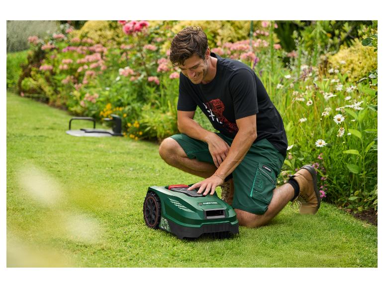 Mann kniet neben einem Mähroboter im Garten