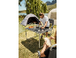 Mann kocht auf einem Campingkocher an einem Klapptisch, mit Zelten und einem See im Hintergrund.