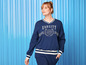 Eine Frau trägt einen blauen Pullover mit 'Varsity' Schriftzug und passende Hosen.
