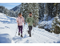 Paar in Winterjacken und Hosen mit Stöcken auf einer Skipiste im verschneiten Wald.