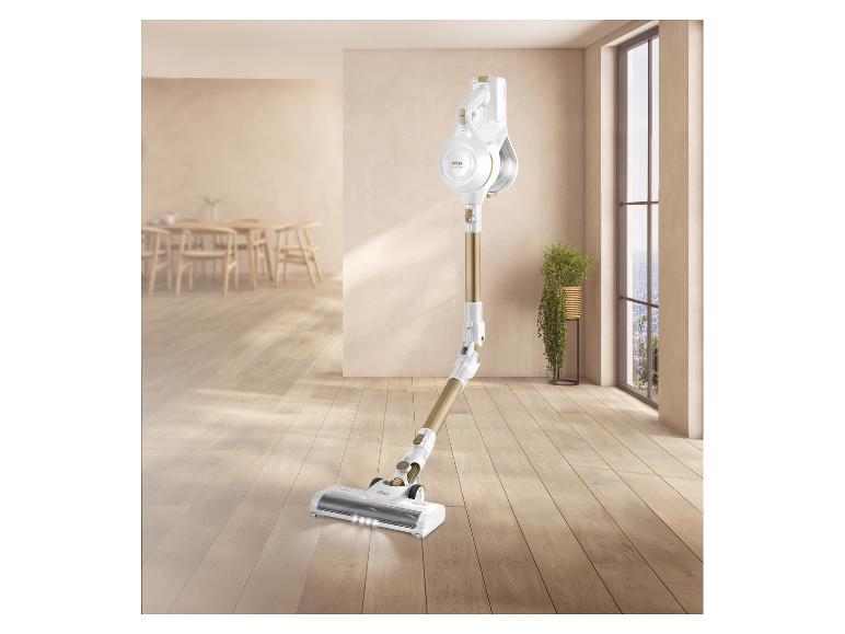 Weißer und goldener Akku-Staubsauger auf Holzboden in einem hellen Raum.