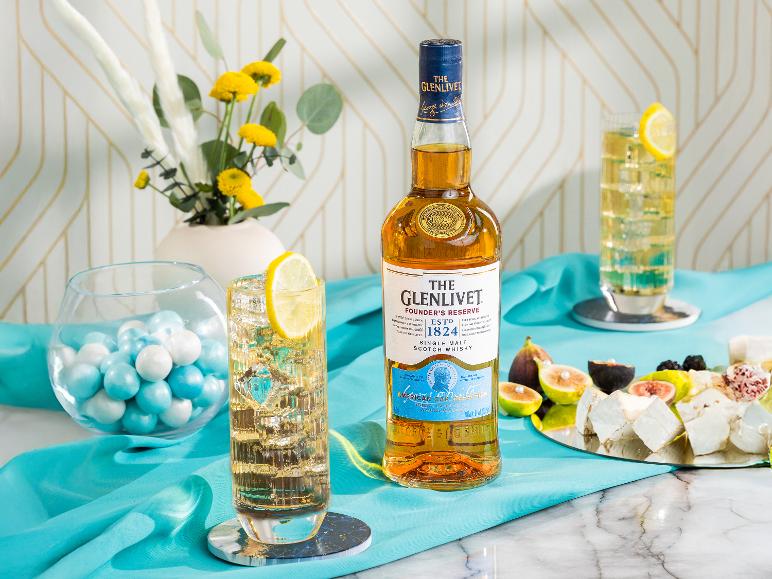 Flasche schottischer Whisky, Gläser mit Eistee und Zitrone, Bonbons und eine Käseplatte.