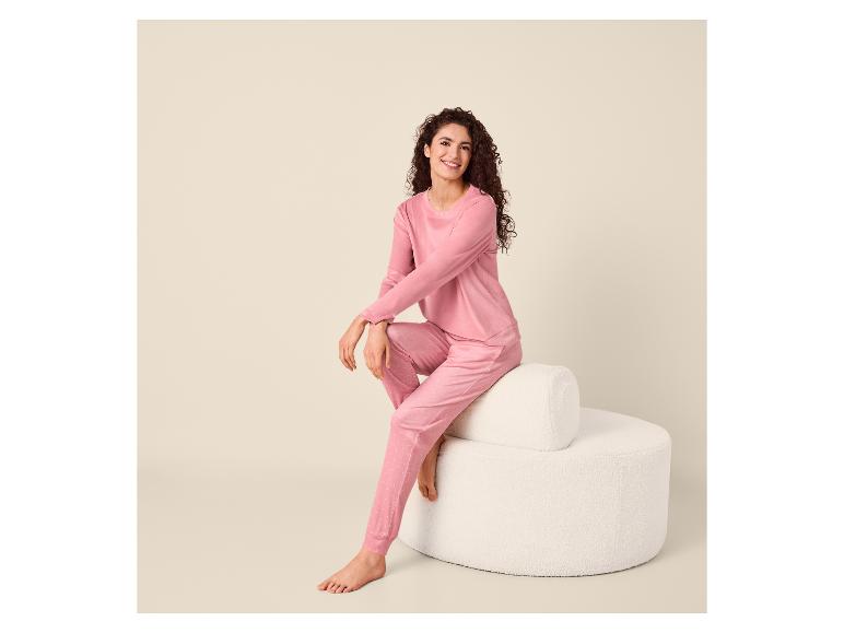 Frau in rosa gepunktetem Pyjama sitzt lächelnd auf einem weißen Hocker.
