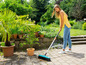Eine Frau fegt Blätter auf einer Terrasse mit einem Besen.