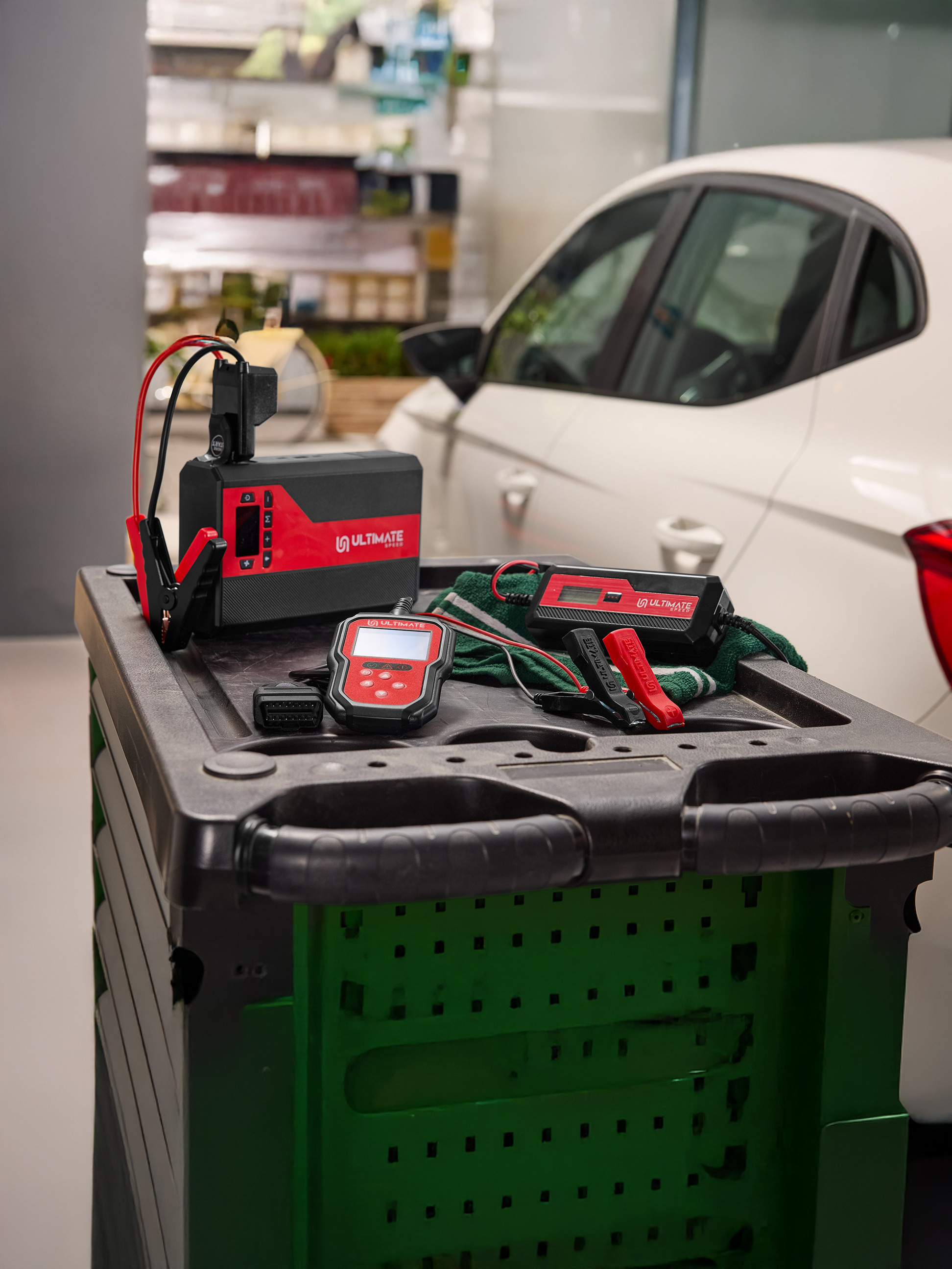 Autobatterieladegerät und Diagnosewerkzeuge auf einem Wagen neben einem weißen Auto.