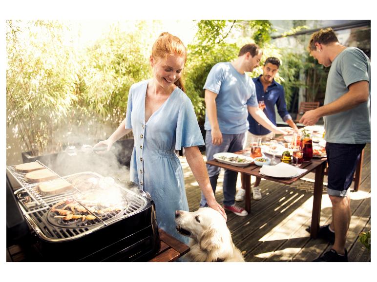 Frau grillt Fleisch und Brot draußen mit Freunden und einem Hund.