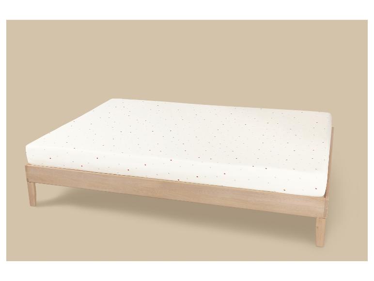 Holzbett mit weißer Matratze mit bunten Punkten auf beigem Hintergrund.