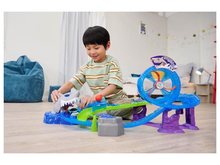 Ein Junge spielt mit einem Hot Wheels Shark Cyclone Spielset auf dem Boden.