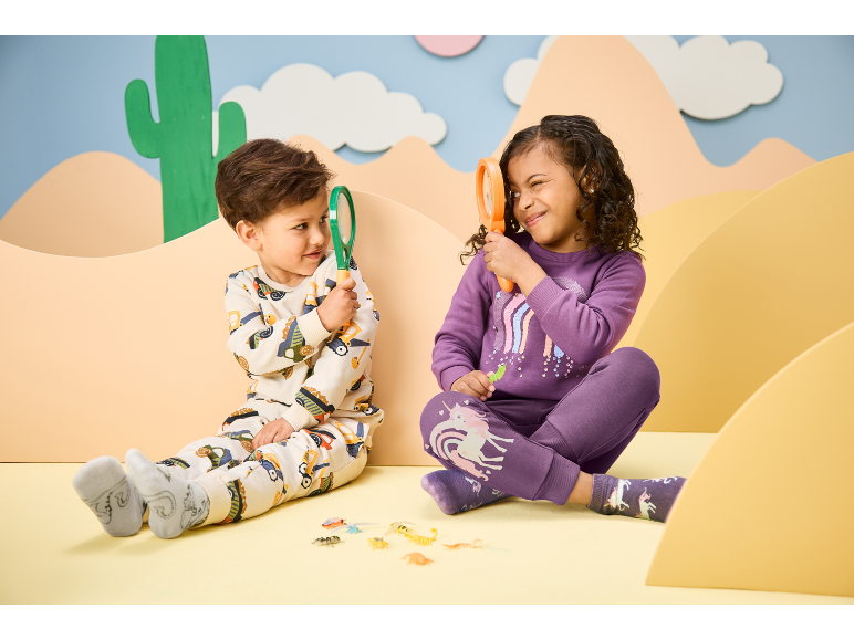 Zwei Kinder in Schlafanzügen mit Tiermotiven, halten Lupen und betrachten Spielzeuginsekten.