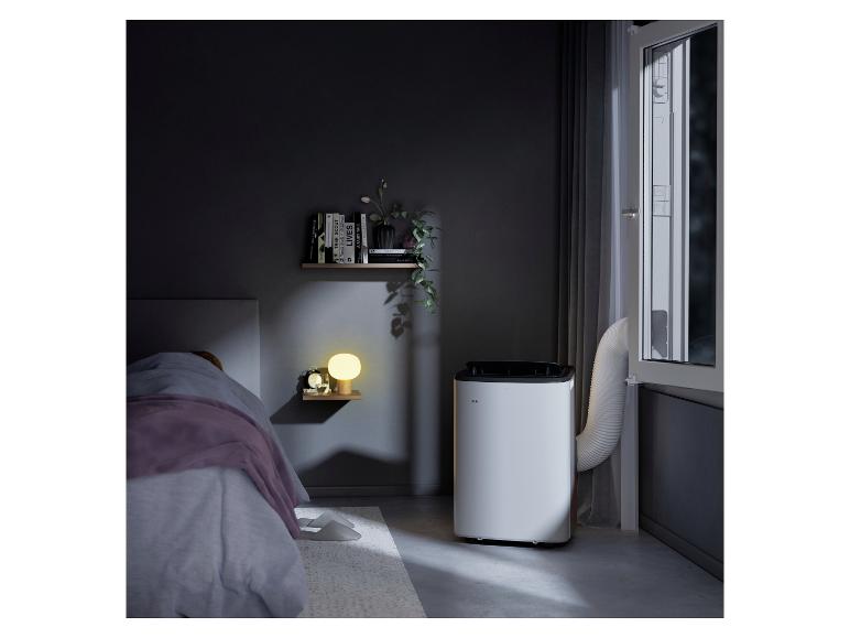 Mobiles Klimagerät im Schlafzimmer mit Bett, Nachttischlampe und Bücherregalen.