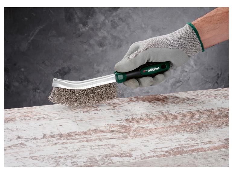 Eine Hand hält eine Parkside Bürste auf einer Holzoberfläche.