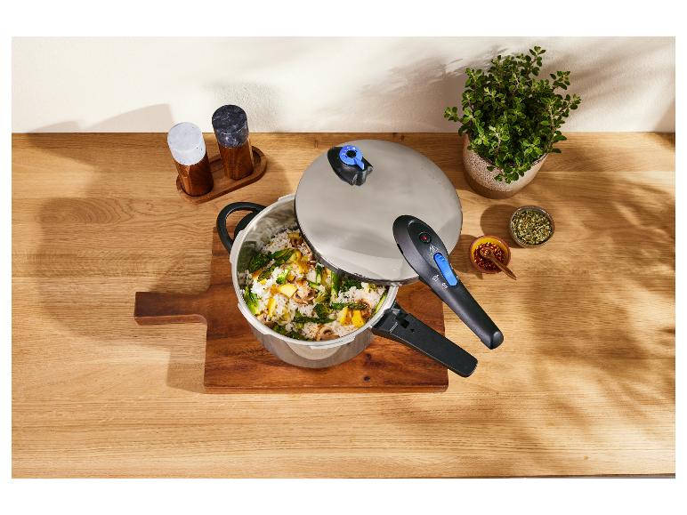 Ein Schnellkochtopf mit Reis und Gemüse, Gewürzen und einer Pflanze auf einem Holztisch.