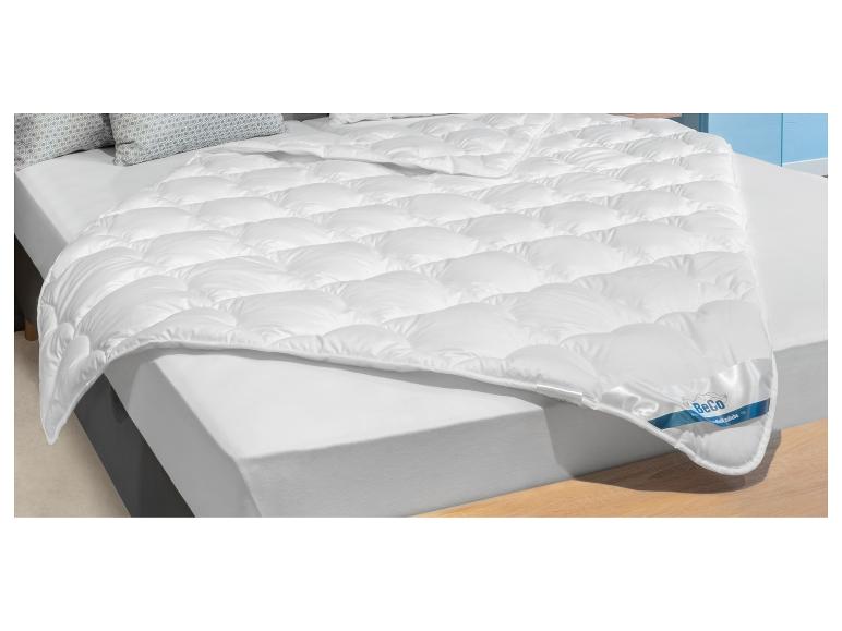 Weiße gesteppte Bettdecke auf einem Bett mit weißem Laken und Kissen mit geometrischem Muster.