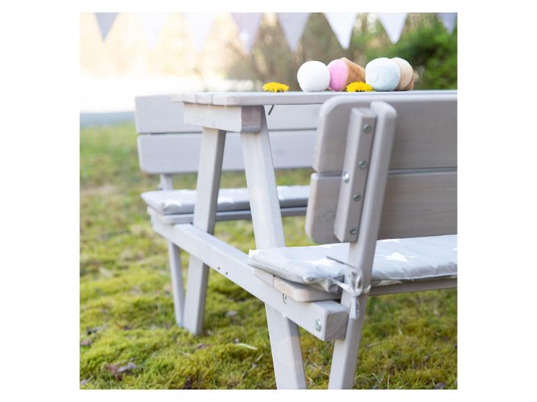 Grauer Picknicktisch mit Bänken und Kissen, dekoriert mit Spielzeugeis und Löwenzahn.