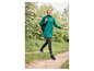 Eine Frau in einer grünen Jacke und schwarzen Leggings geht auf einem Weg im Wald entlang.