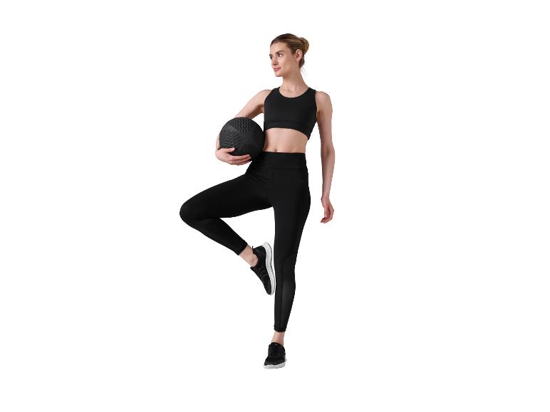 Frau in schwarzer Sportkleidung hält einen Medizinball, steht auf einem Bein.