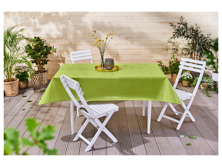 Ein grüner Tischdecken auf einem Holztisch mit weißen Klappstühlen.
